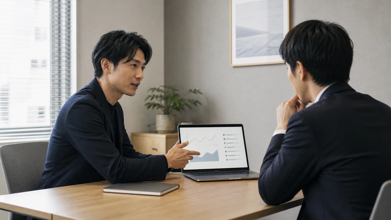 1対1のミーティングでノートPCの資料を指し示しながら説明する様子