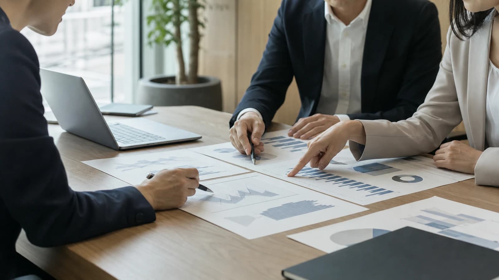 会議室で数人がグラフ資料を指し示しながら議論する手元と上半身